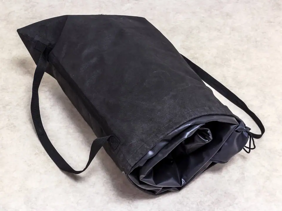 A deflated air mattress packed into its black drawstring carry bag on a carpet