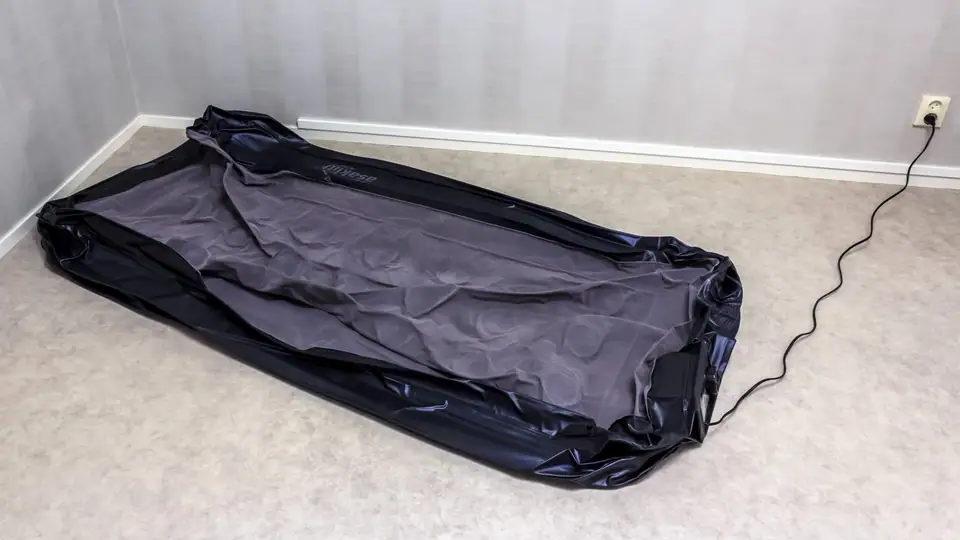 Deflated air mattress lying flat on a carpet with its power cord