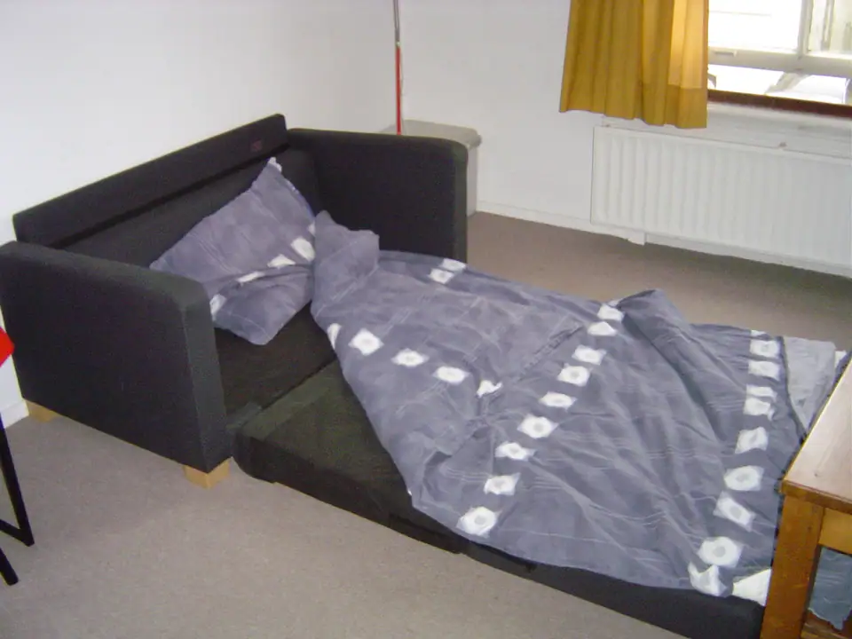 Dark sofa bed folded out and made up with a patterned duvet and pillow