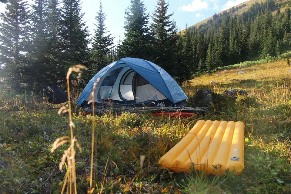 Dome tent in a meadow with a yellow inflatable mattress beside it